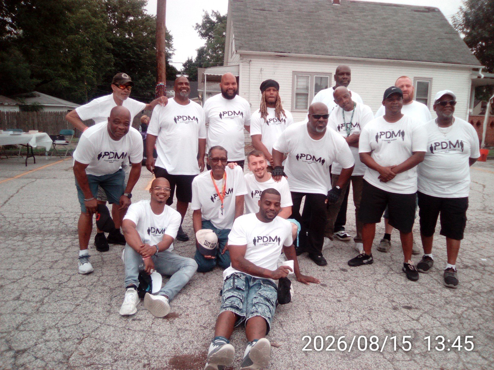 A group of men who identify as the Purpose Driven Men out of Cleveland Ohio standing together at a community outreach event with their logo in black on white t-shirts